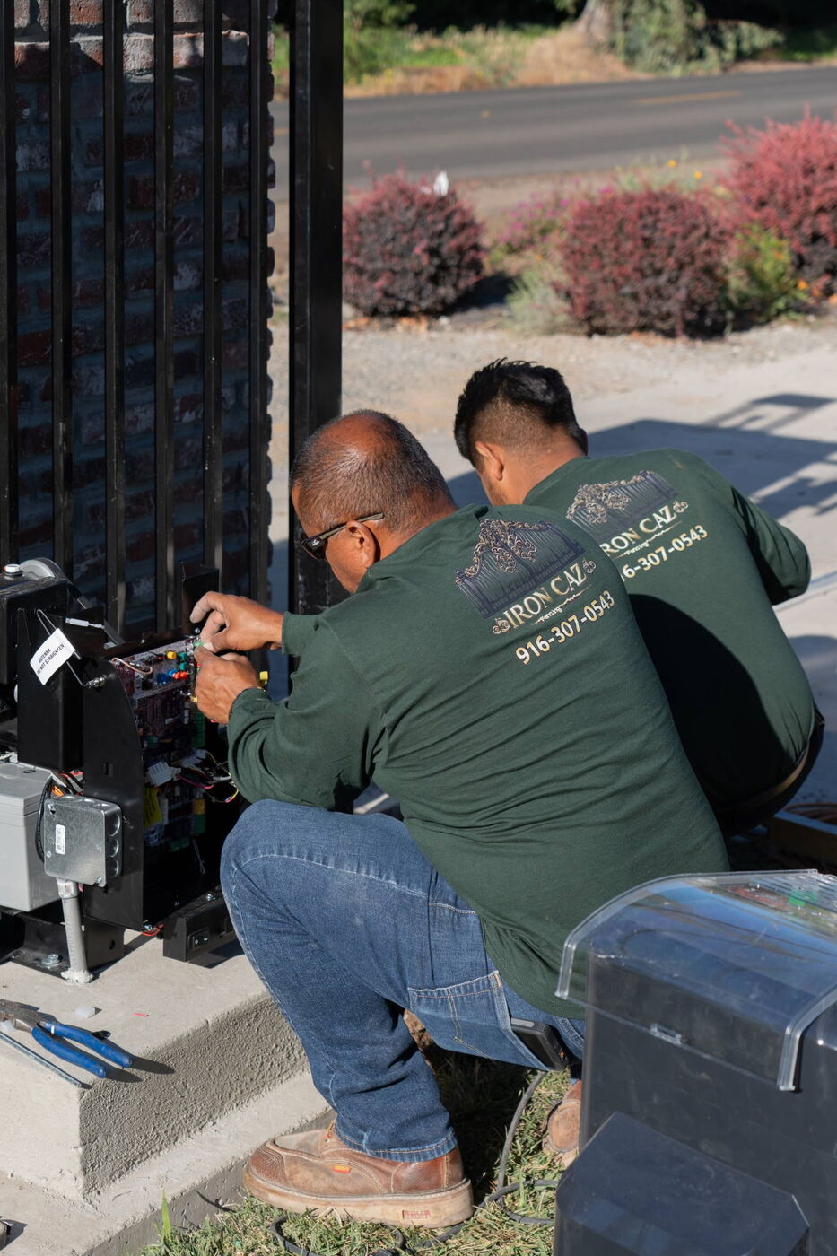 Iron Caz technicians wiring an automatic gate opener control board on a steel driveway gate