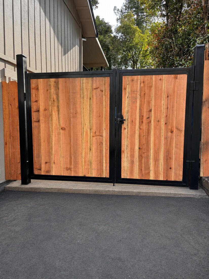 Double redwood gate in a black steel frame between two structures