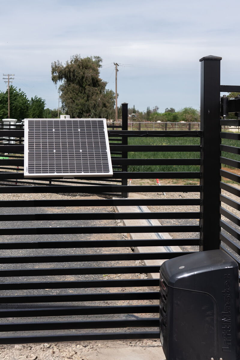 Solar panel powering a LiftMaster automatic sliding gate opener on a black slat gate
